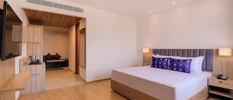 A modern hotel room with a large bed, bedside tables, a desk, and a seating area with a sofa and chairs.