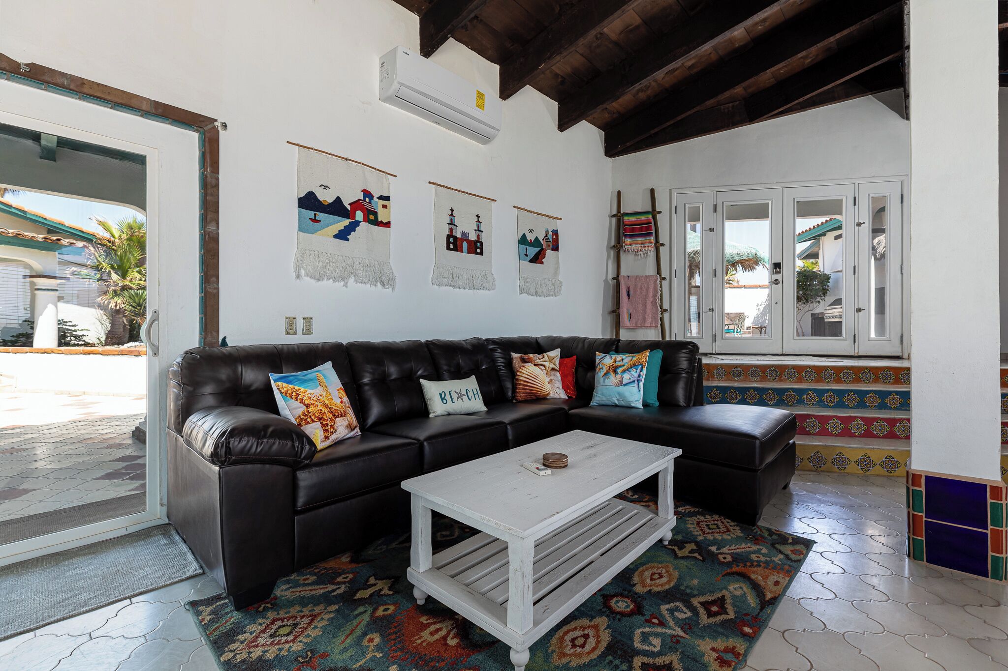 A living room with a black leather sofa, a white coffee table, and colorful wall art.