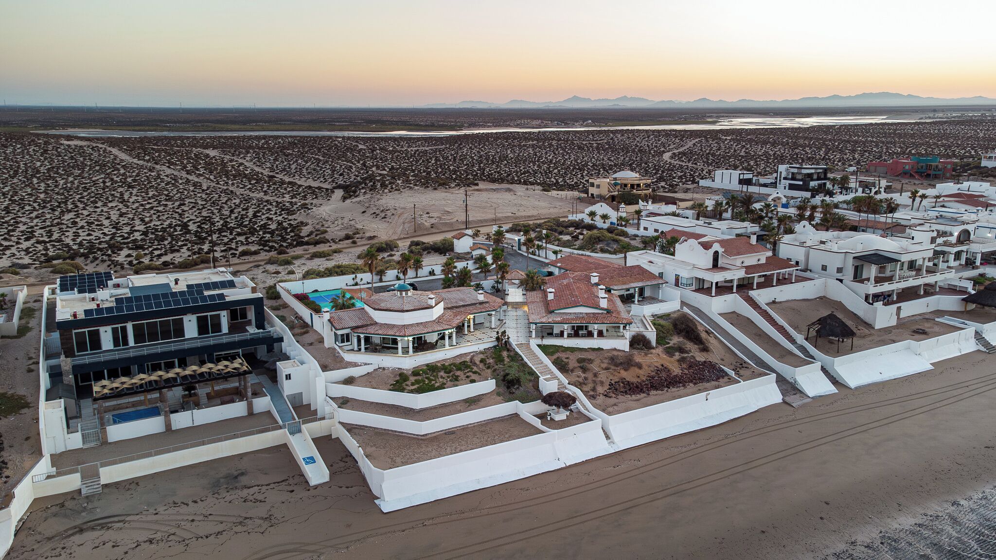 An aerial view of a coastal residential area with modern houses, a swimming pool, and a beach.
