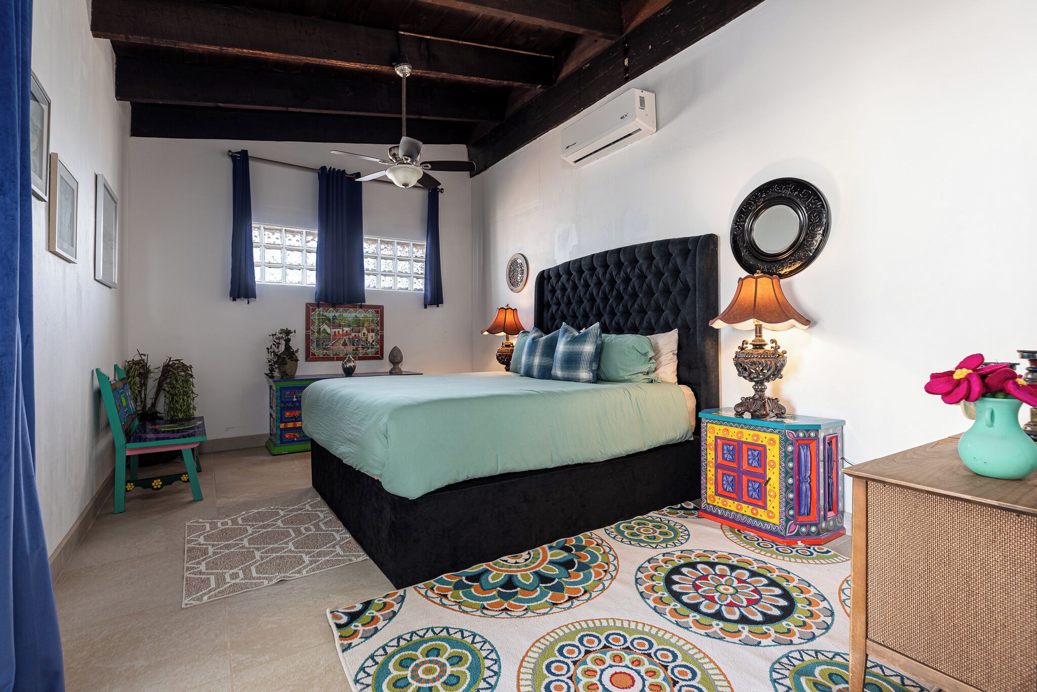 A bedroom with a bed, a ceiling fan, a window with curtains, a wall-mounted air conditioner, and a decorative lamp.