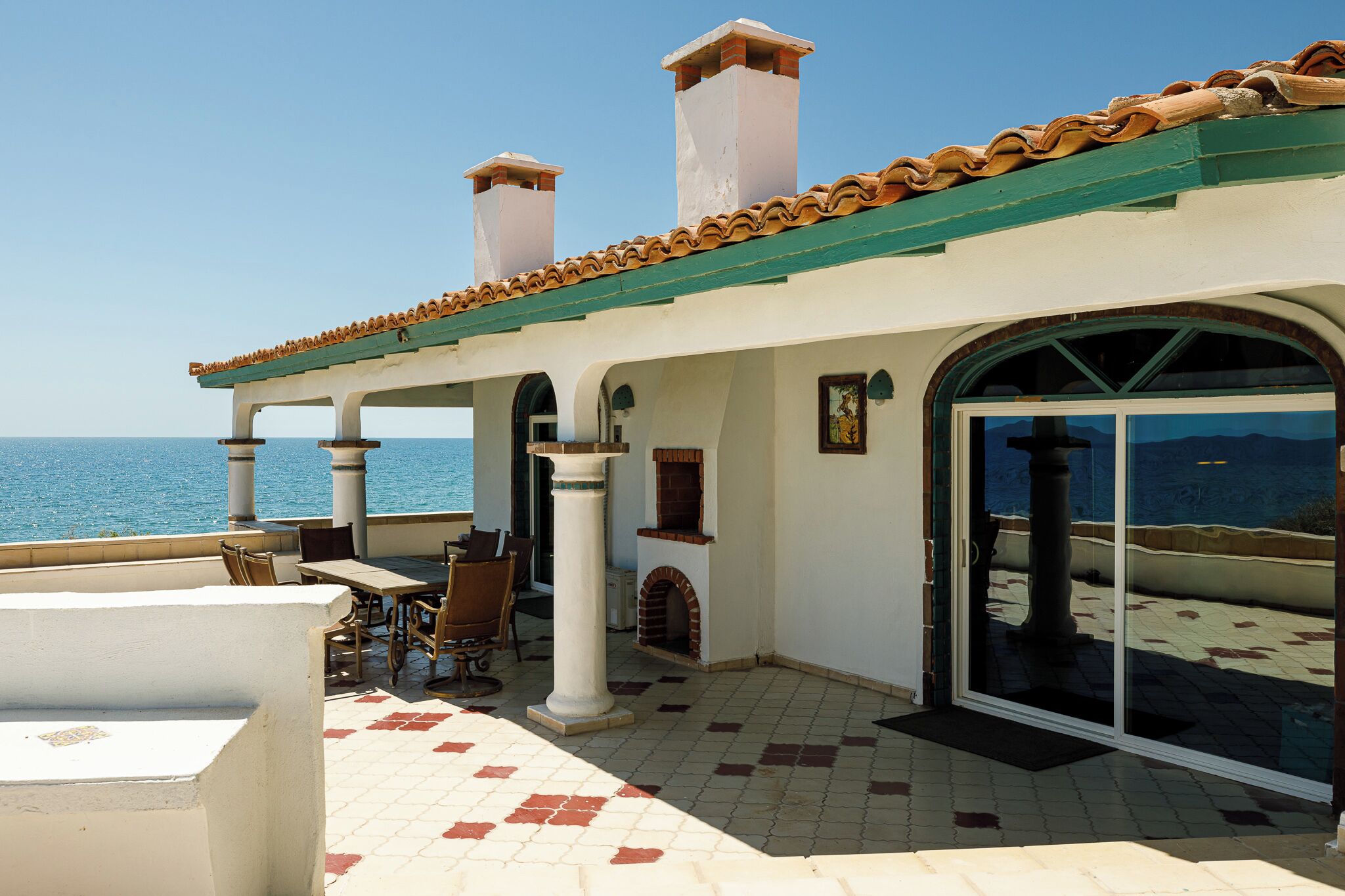 Une terrasse avec vue sur la mer, un espace salon couvert et une porte vitrée donnant sur l’intérieur.