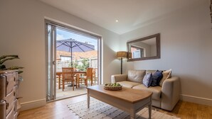 Een woonkamer met een bank, salontafel en een schuifdeur die leidt naar een terras buiten met een tafel en stoelen.