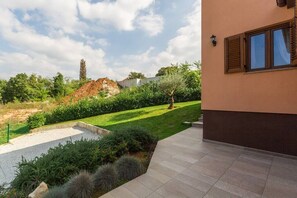 A modern house with a paved patio, a well-maintained lawn, and a stone wall.