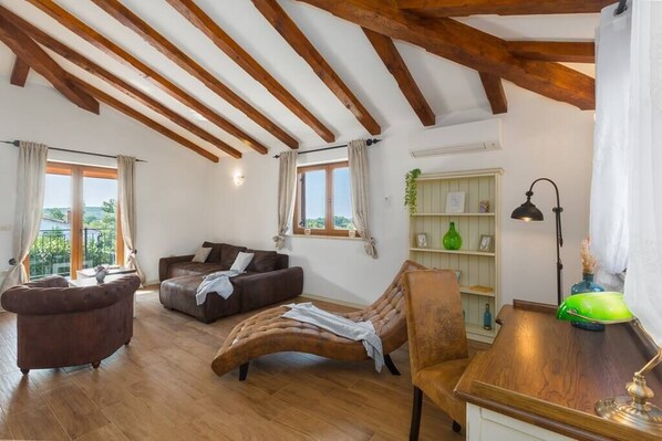A spacious living room with wooden beams, a brown leather sofa, a chaise lounge, and a wooden coffee table.