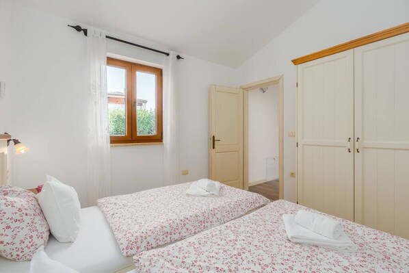 A bedroom with two beds, a window, a door, and a wardrobe.