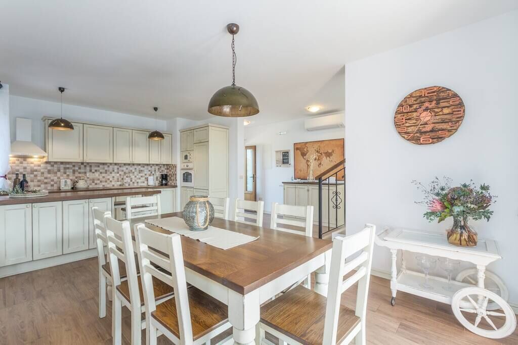 A modern kitchen with white cabinetry, a wooden dining table, and pendant lighting.