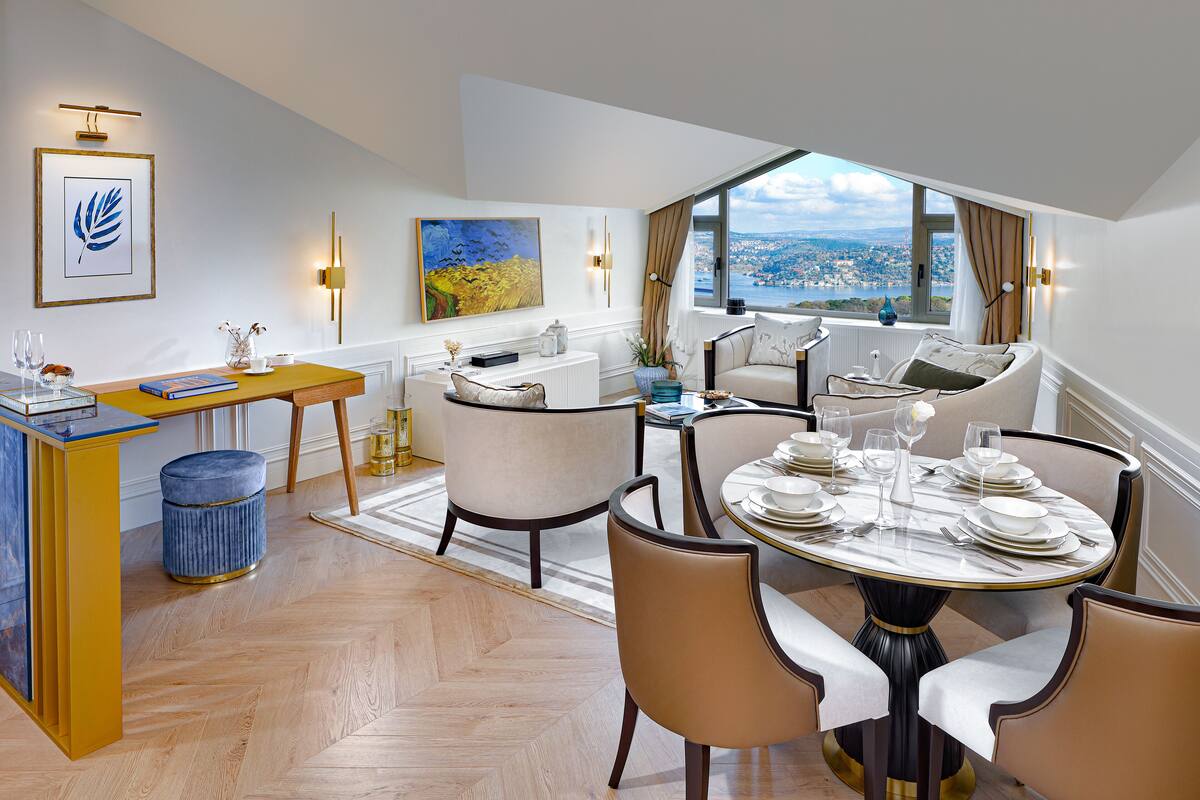 Un coin repas avec une table ronde dressée pour six personnes, entourée de six chaises. Une grande fenêtre offre une vue sur le paysage urbain.