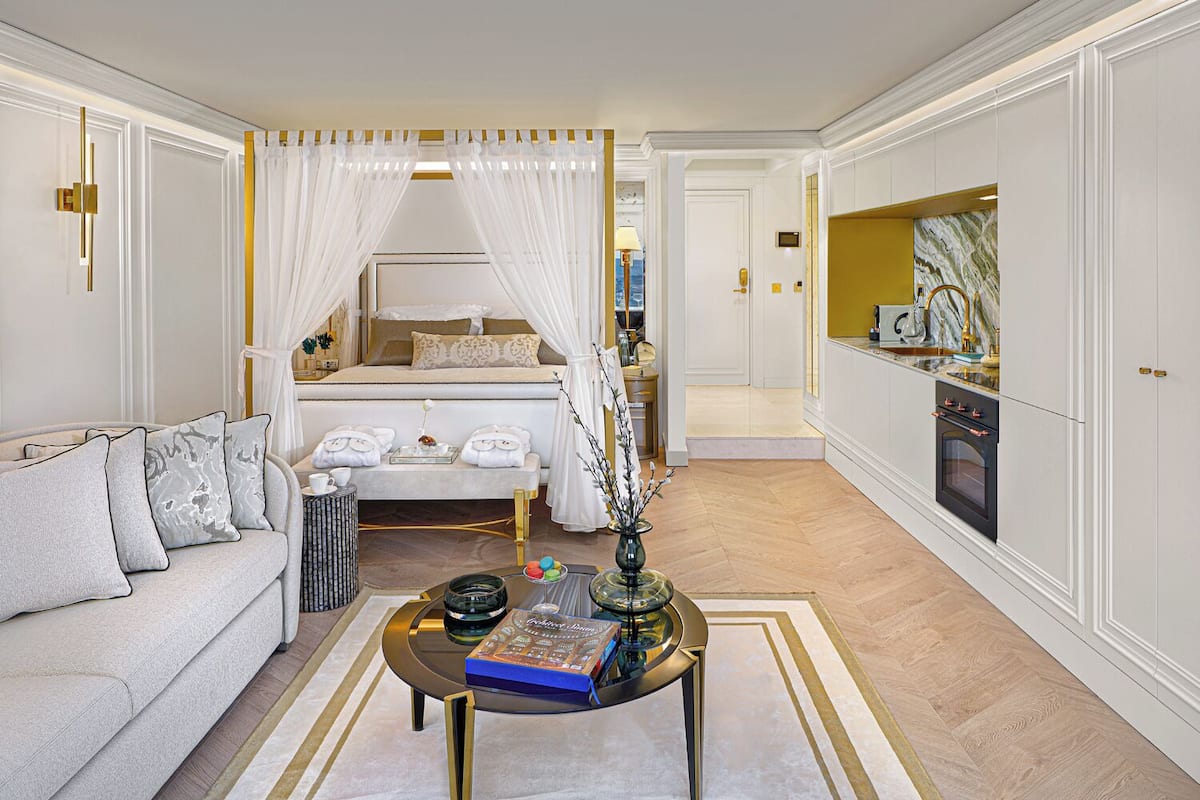 Une chambre à coucher luxueuse avec un lit à baldaquin, un coin salon doté d’une table basse et une cuisine avec des plans de travail en marbre.