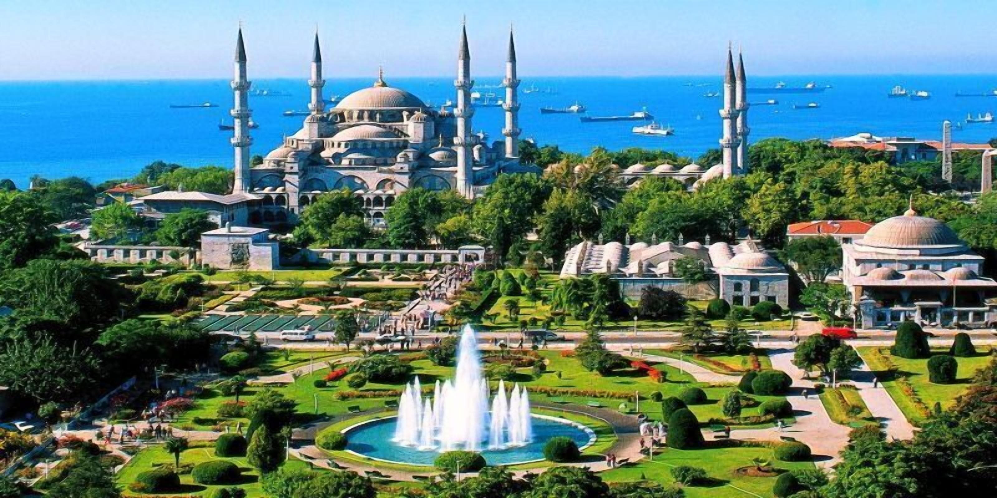 A large mosque with multiple minarets and domes, surrounded by lush gardens and a central fountain.