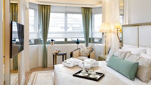 Een hotelkamer met een bed, een televisie, een nachtkastje, een lamp en uitzicht op de stad door het raam.