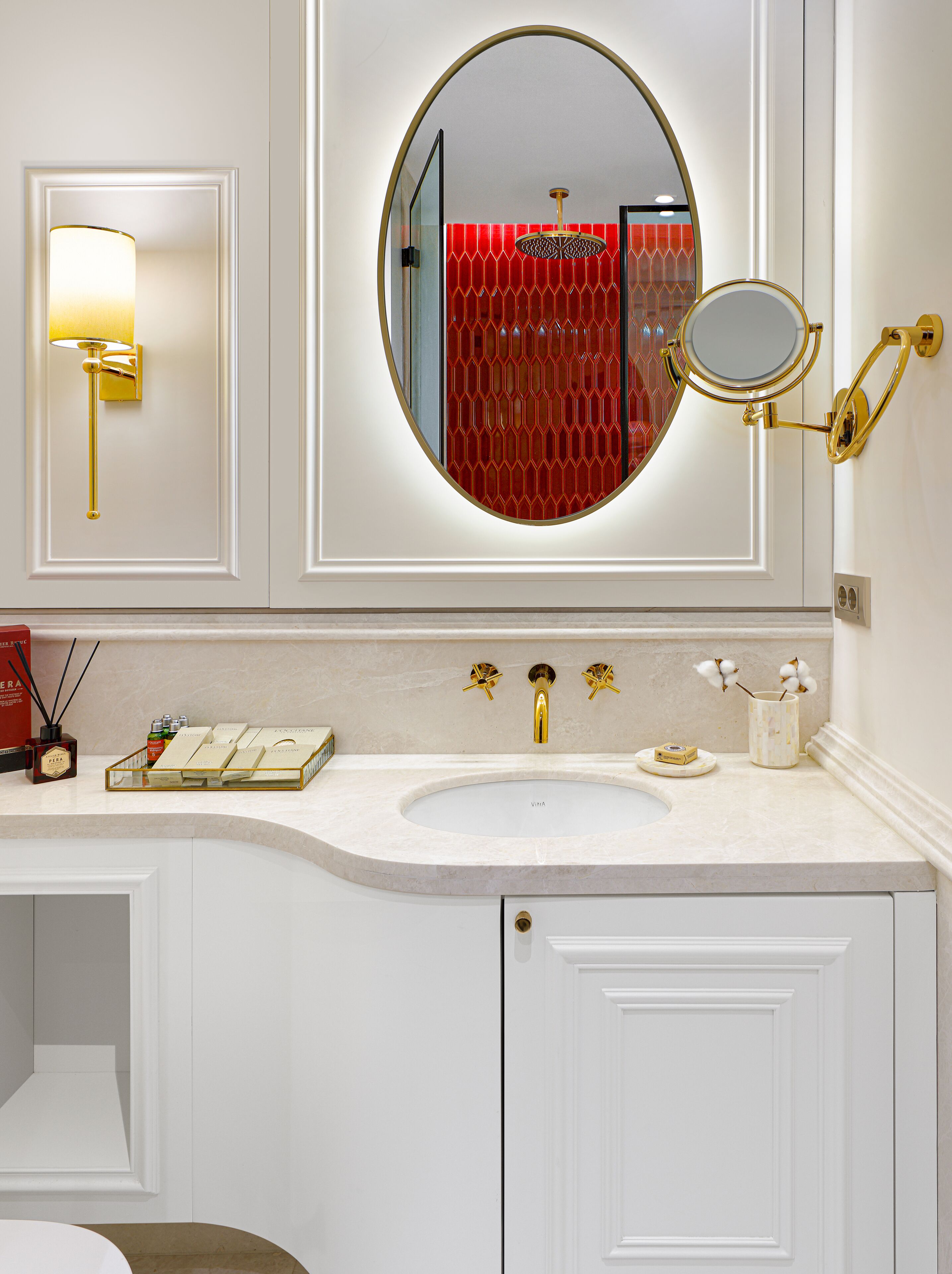 A bathroom with a white vanity, a gold faucet, a round mirror, and a red decorative panel.