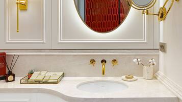 A bathroom with a white vanity, a gold faucet, a round mirror, and a red decorative panel.