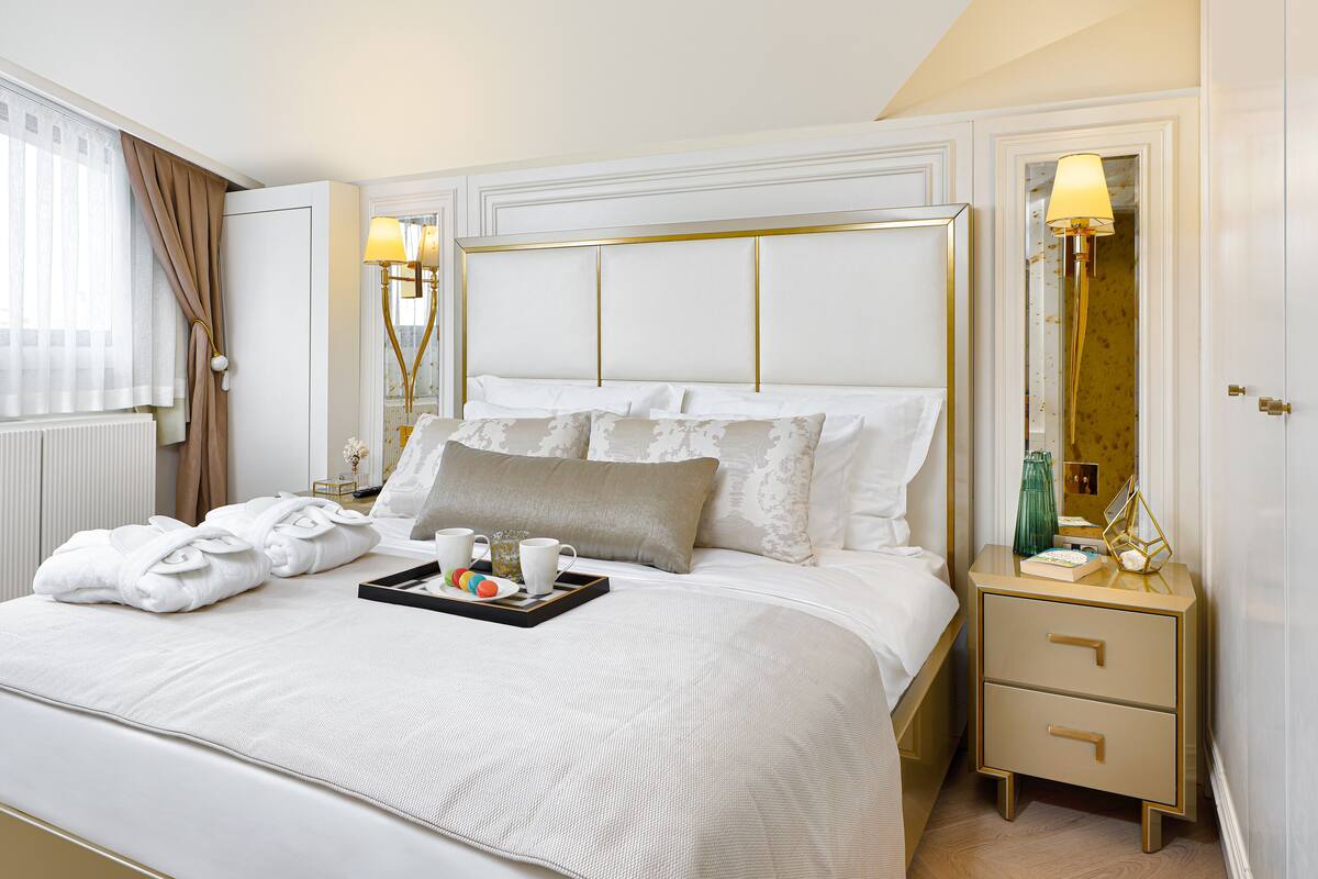 Un lit bien fait, avec un plateau contenant des articles pour le petit-déjeuner, une table de chevet avec une lampe et un miroir accroché au mur.