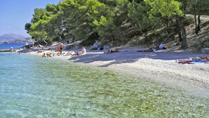 Ein Strand mit klarem Wasser, sonnenbadenden Menschen und Bäumen.
