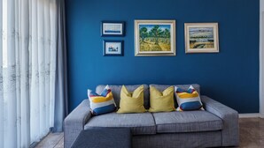 Ein Wohnzimmer mit blauer Wand, einem grauen Sofa mit bunten Kissen und drei gerahmten Bildern.