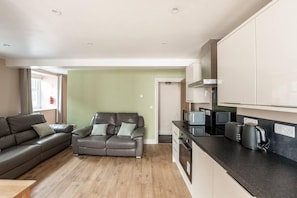 A compact living space with a sofa, kitchenette, and a door leading to another room. - Beautiful 2-bed House in Egremont Milo's Place (Egremont)
