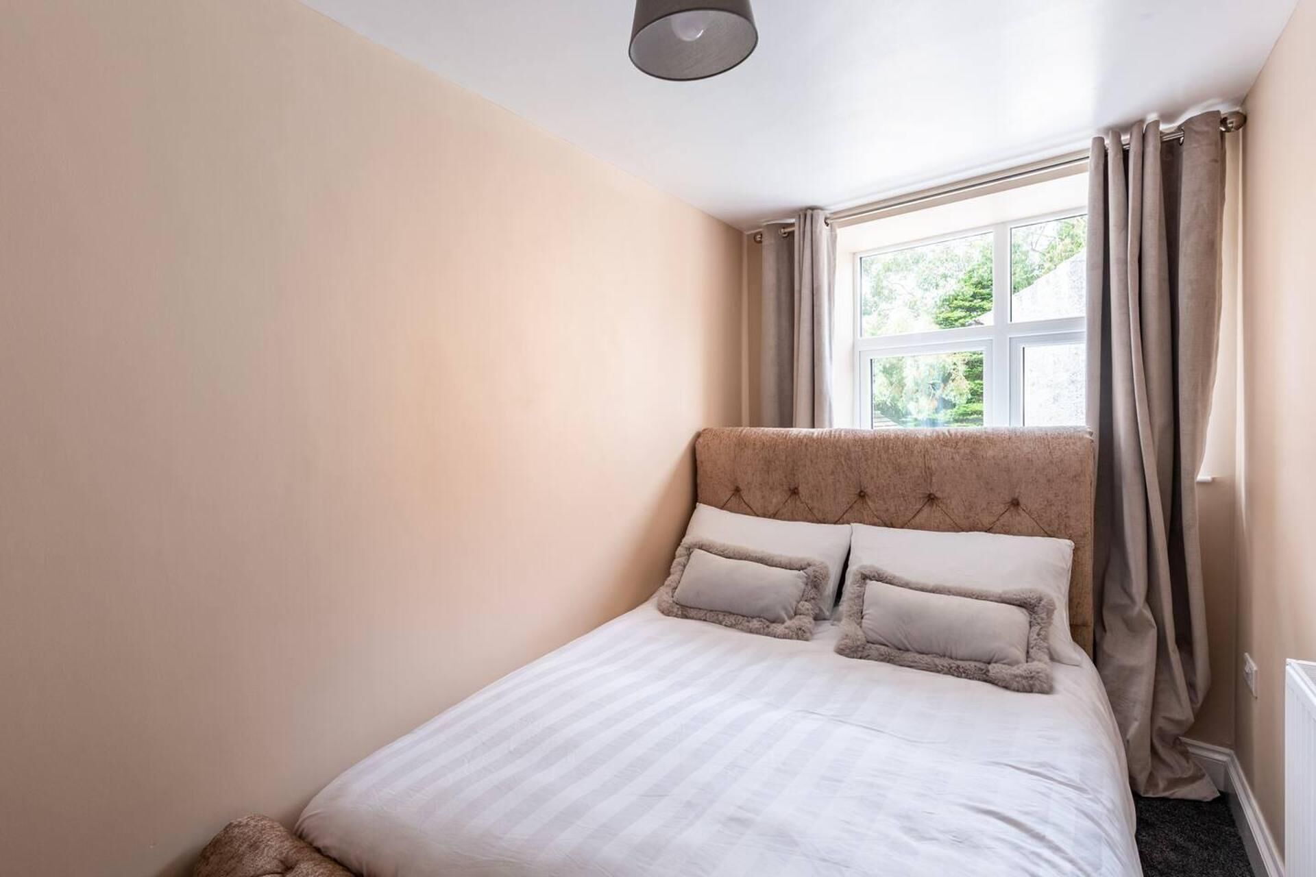 A bedroom with a bed, a window with curtains, and a light fixture.
