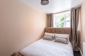 Une chambre à coucher avec un lit, une fenêtre avec des rideaux et un luminaire.