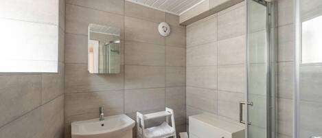 Un baño moderno con lavamanos, espejo, toallero, inodoro y cabina de ducha de vidrio.