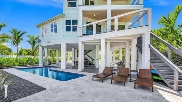 Una casa de dos pisos con piscina, mobiliario exterior y una escalera.