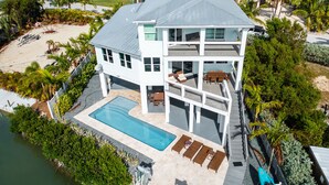 Una casa de dos pisos con piscina, mobiliario exterior y vista al océano.
