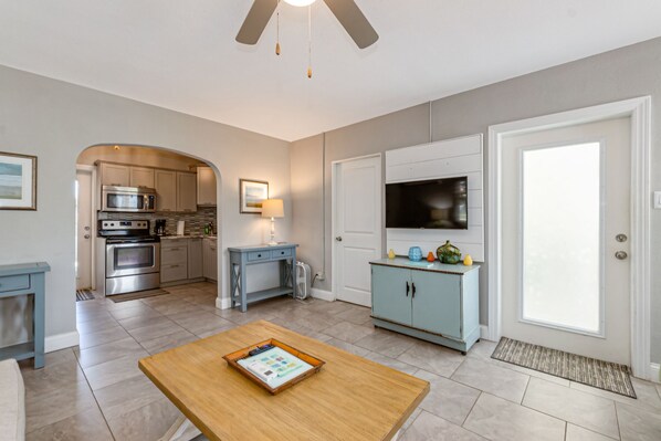 A modern kitchen with stainless steel appliances, a dining area with a wooden table, and a light blue cabinet. - Beautiful downtown Melbourne Beach renovated apartment one block from the beach! (Melbourne Beach)