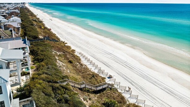 A coastal hotel with a long beachfront, a staircase leading to the beach, and a clear view of the ocean.