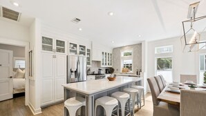 A modern kitchen with white cabinetry, a central island with stools, and a dining area with a table and chairs.