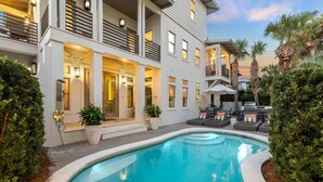 A modern two-story house with a swimming pool, outdoor seating, and a well-lit entrance.