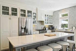 Enjoy cooking in this well-equipped kitchen with a large island, bar stools, stainless steel appliances, and ample storage.