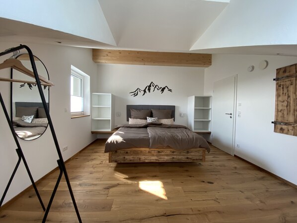 A bedroom with a large bed, wooden beams, a wardrobe, and built-in shelving.