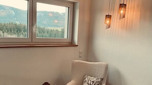 A cozy room with a plush armchair, a small wooden stool, and a round rug. - Das Franz 1 (Weitnau)