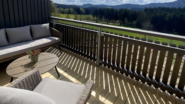 A wooden deck with outdoor furniture, including a sofa and chairs, overlooking a scenic landscape with mountains and trees. - Das Franz 1 (Weitnau)