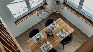 A dining area with a wooden table set for four, two pendant lights, and large windows with a view of a snowy landscape. - Das Franz 1 (Weitnau)