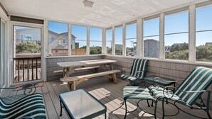 A covered outdoor area with a wooden picnic table, green striped chairs, and a glass table. - Serenity Shores: 125ft. to Beach | Private Pool (Southern Shores)