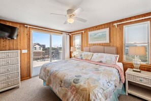 Ein Schlafzimmer mit einem Bett, einem Deckenventilator, einem Fernseher, einem Nachttisch aus Weidwerk und Blick ins Freie.
