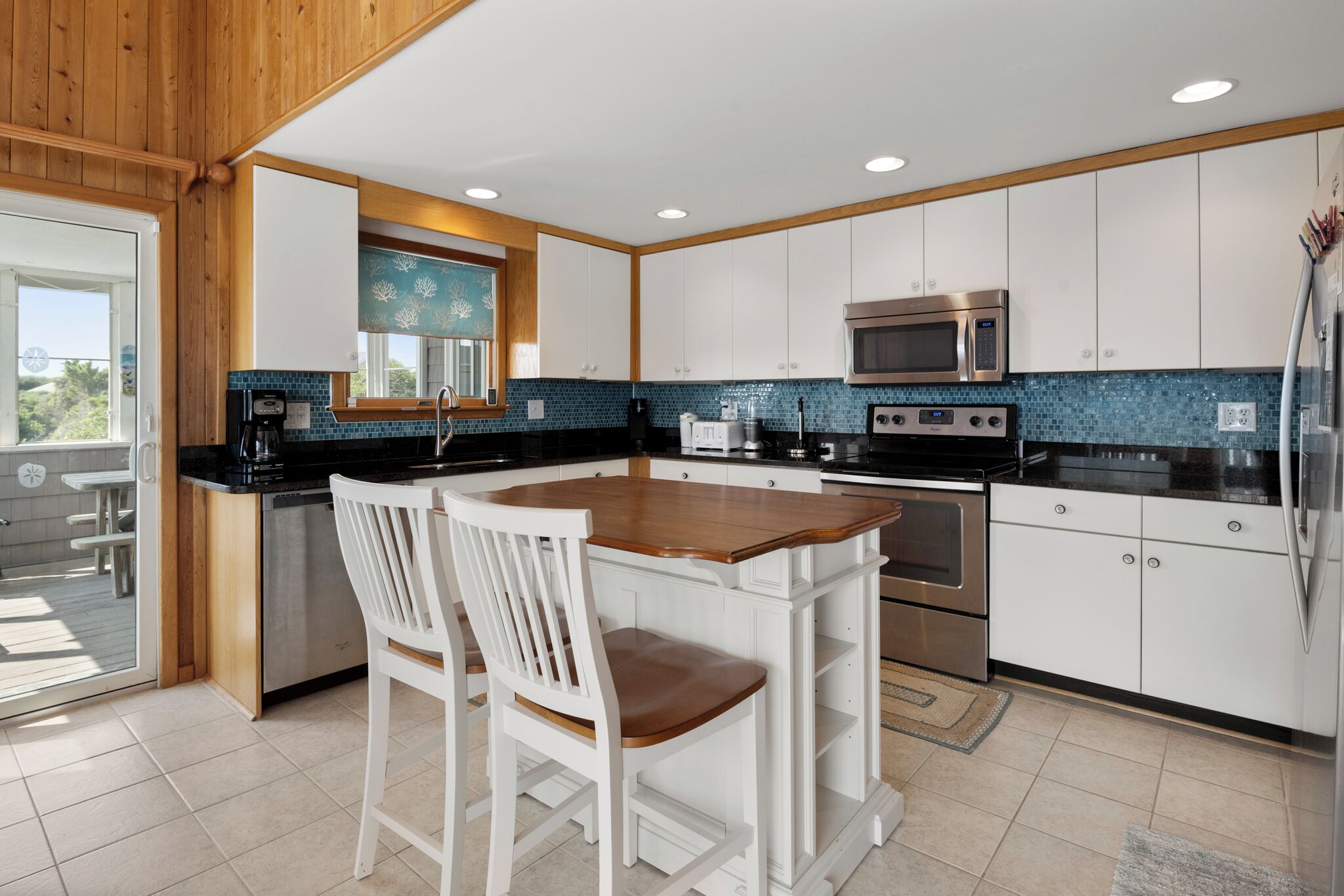 A modern kitchen with white cabinets, a wooden island, stainless steel appliances, and a view to the outside.