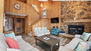 A spacious living room with a stone fireplace, a staircase, and a cozy seating area. - Serenity Shores: 125ft. to Beach | Private Pool (Southern Shores)