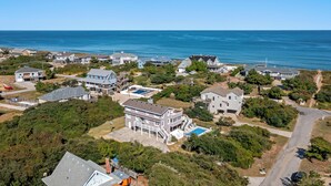 An aerial view of a coastal residential area with houses, a swimming pool, and a clear view of the ocean. - Serenity Shores: 125ft. to Beach | Private Pool (Southern Shores)