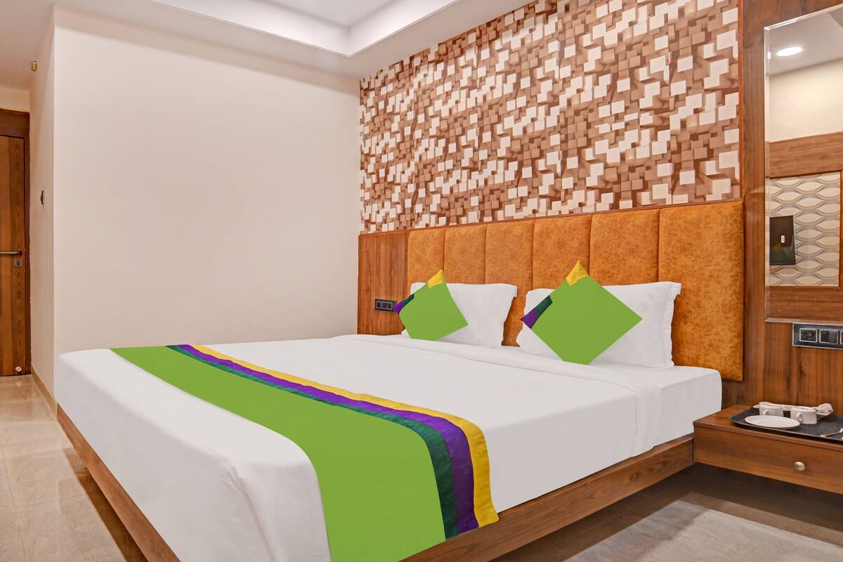 A modern hotel room with a wooden headboard, a large bed with white bedding, and a decorative wall panel.