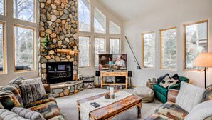 A cozy living room with a stone fireplace, large windows, and comfortable seating. - Windflower Retreat: Beautiful Dog Friendly Home (Frisco)
