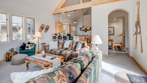 A spacious living room with a high ceiling, a large sofa, a coffee table, and a fireplace. - Windflower Retreat: Beautiful Dog Friendly Home (Frisco)