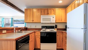 Una cocina con armarios de madera, un microondas blanco, una estufa negra y un refrigerador blanco.