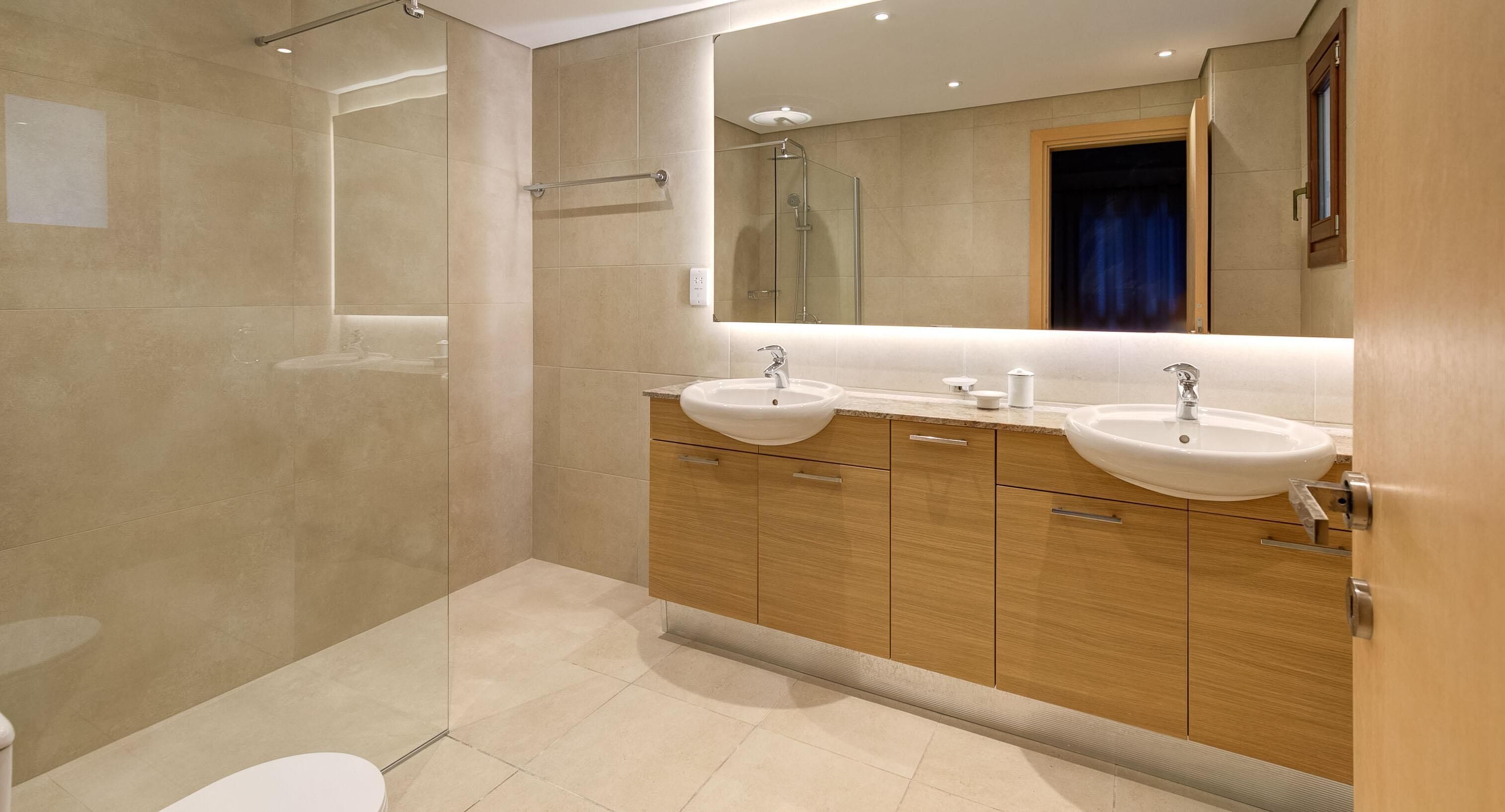 A modern bathroom with two sinks, a glass shower enclosure, and wooden cabinetry.