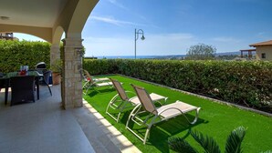 A patio with a table and chairs, a lawn, and a view of the sea. - Apartment BH01 - Anthos (Kouklia)
