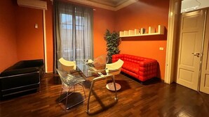Une pièce comprenant une table à manger, des chaises, un canapé rouge, une petite plante et une bibliothèque.