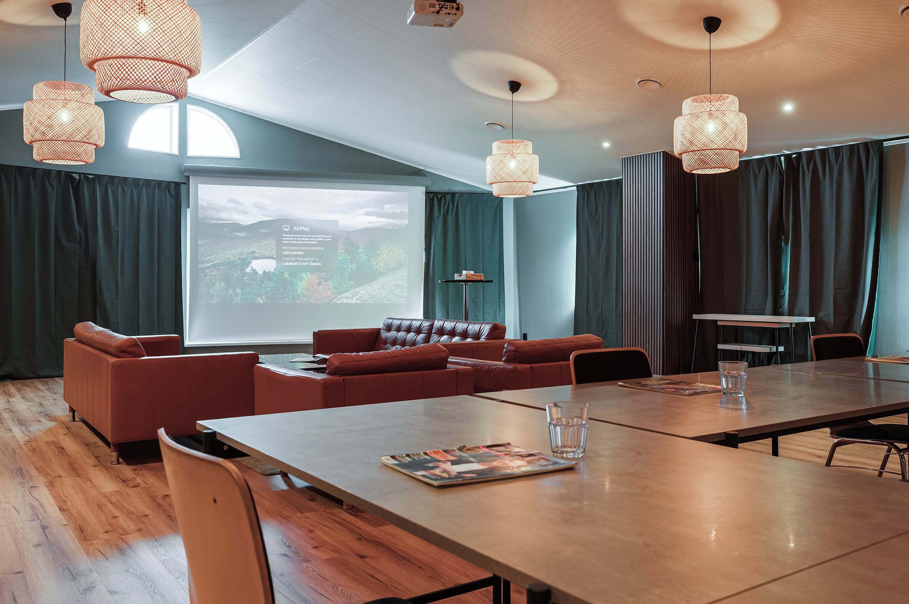 Une salle de conférence dotée d’une grande table, de canapés en cuir rouge et d’un écran de projection sur lequel est affiché un paysage.