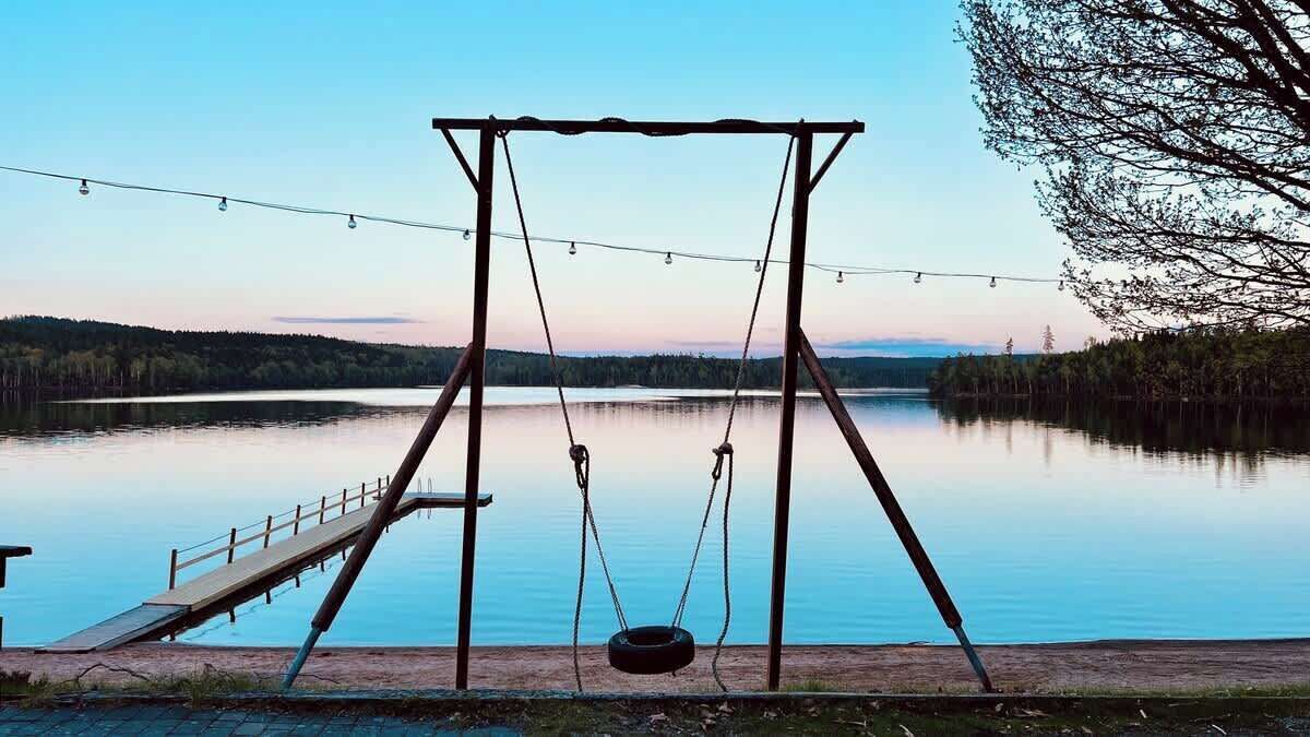 A swing set by a calm lake with a wooden deck and a metal frame.