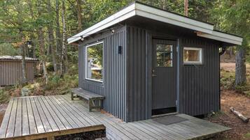 En liten, mörk stuga med en träveranda och ett enda fönster.