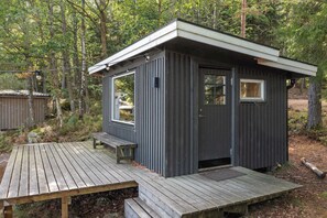 A small, dark-colored cabin with a wooden deck and a single window.